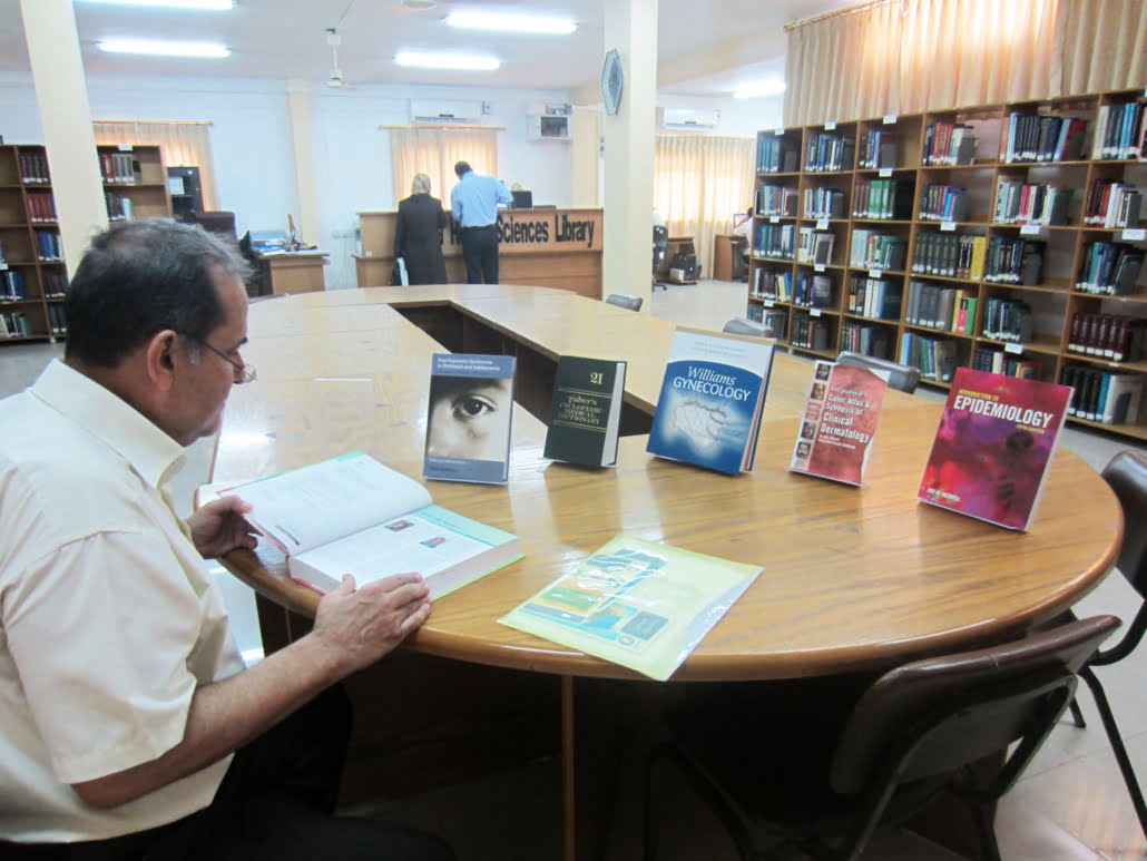 Mannlig person sitter ved bord med bøker og leser og studerer. Det er del av et bibliotek. Foto. 
