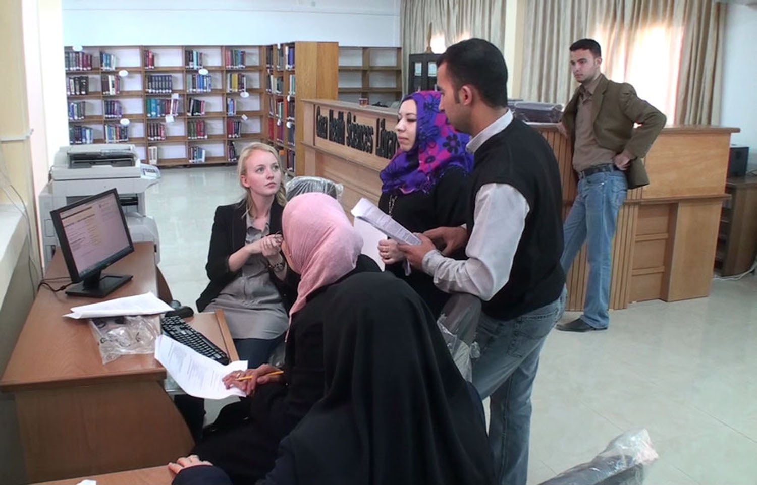 Fire personer i samtale foran en datamaskin på et bibliotek. Opplæringssituasjon. Foto.