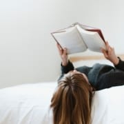 Kvinne ligger på en seng med bok i hendene og leser. foto.