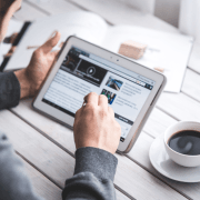 mann holder ipad i hendene, sitter ved et bord med en kaffekopp. illustrasjonsfoto.