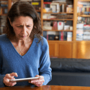 kvinne leser på ipad, bekymret blikk. Bokhyller i bakgrunnen. illustrasjonsfoto.