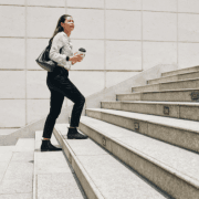 kvinne med svart bukse og hvit skjorte med engangskopp i hånden går oppover betongtrapp. foto.