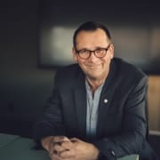 portrett ola eiksund (mann sitter ved bord, smiler, foldede hender foran seg). foto.