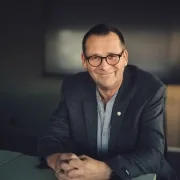 portrett ola eiksund (mann sitter ved bord, smiler, foldede hender foran seg). foto.