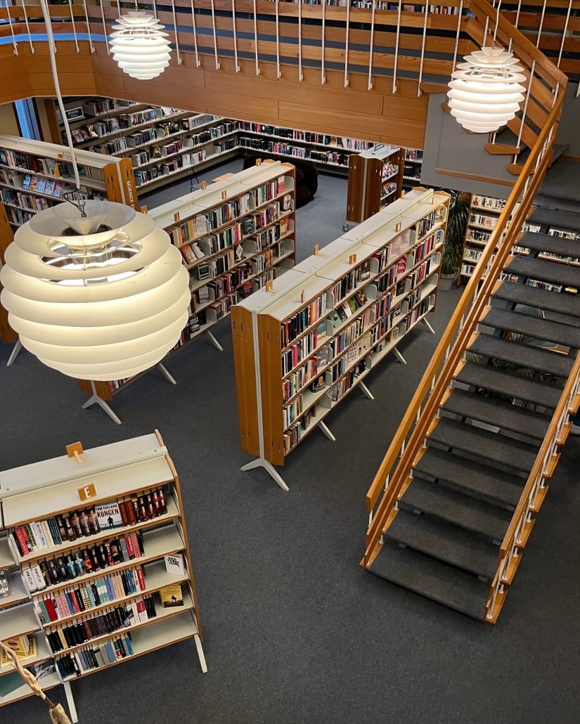 bildet viser rekker med hyller med bøker i to etasjer i et bibliotek, samt en trapp med gelender på begge sider som går fra den ene til den andre etasjen. trappene og gulvet er lagt med teppe i samme farge, og lokalet er dempet belyst. foto. 