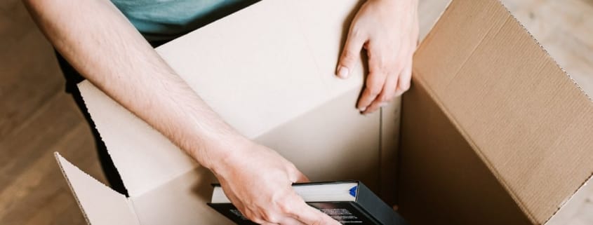 utsnitt av person som legger bøker ned i pappeske.