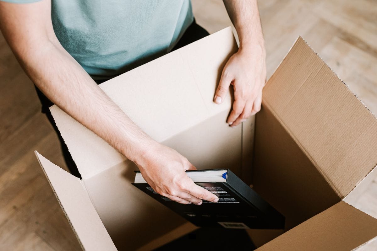 utsnitt av person som legger bøker ned i pappeske.