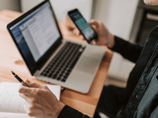 person foran datamaskin med telefon i en hånd og blyant i en annen.illustrasjonsfoto