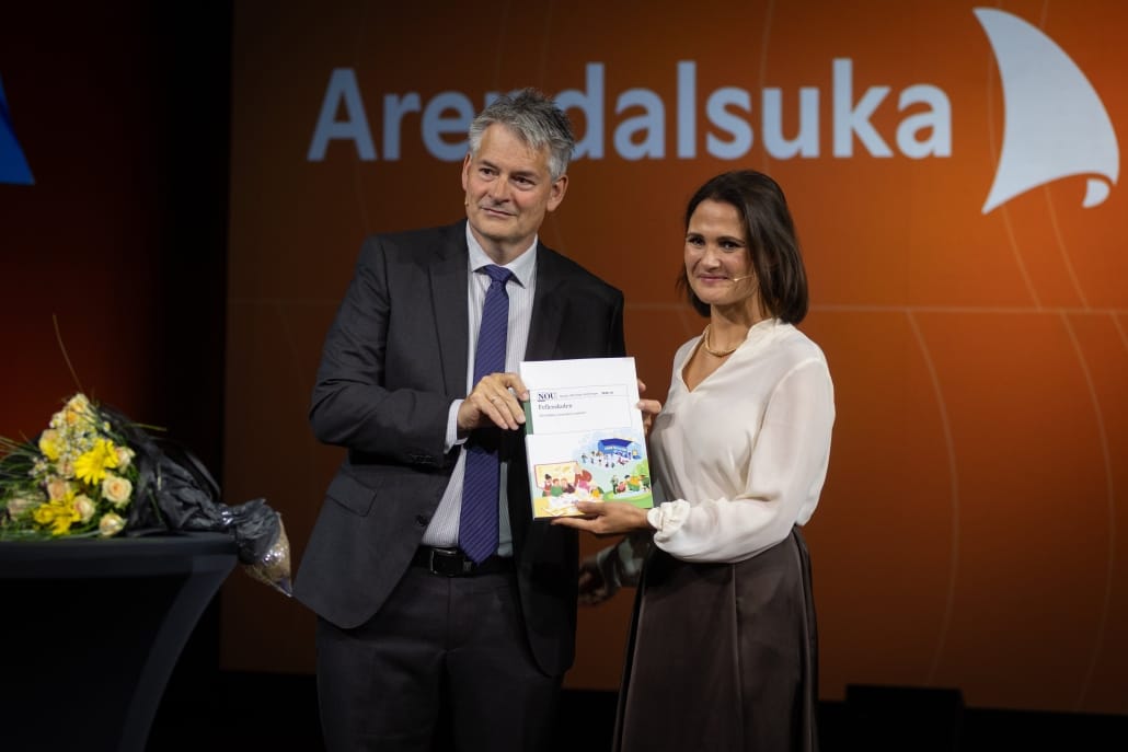 To personer ser mot et publikum (ikke i bildet) mens de begge holder i fellesskolerapporten omtalt i teksten. Personene på bildet er utvalgsleder Bjørn Haugstad og kunnskapsminister Kari Nessa Nordtun.